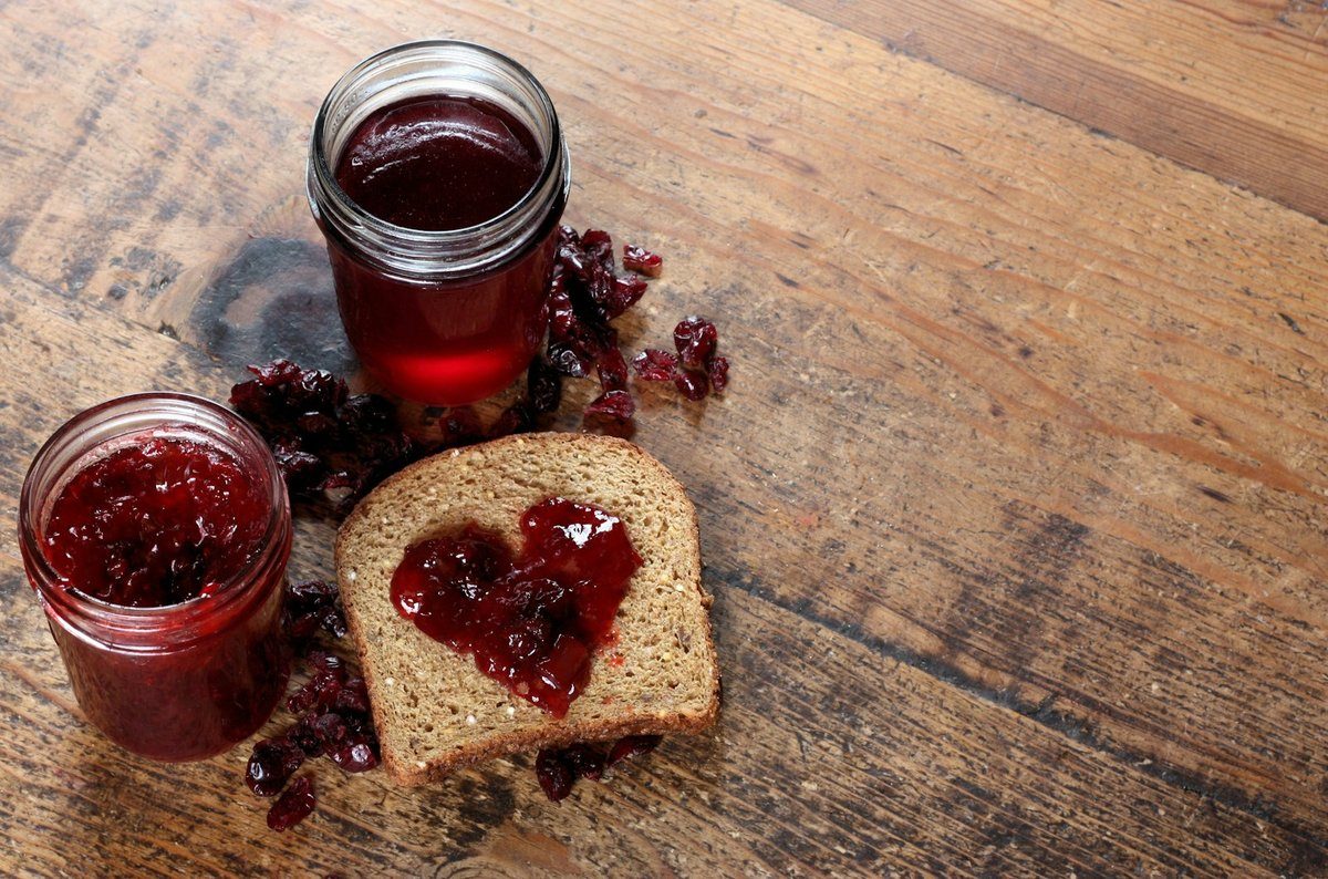 Deux pots de confiture posés à côté d'une tartine sur une planche en bois